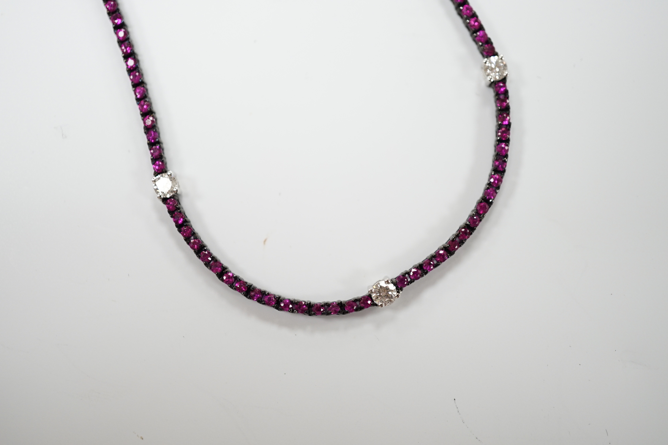 A modern blackened 18k, ruby and diamond line cluster set necklace, 42cm, gross weight 10.3 grams.